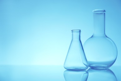 Empty flasks on mirror surface against light blue background, space for text. Laboratory equipment