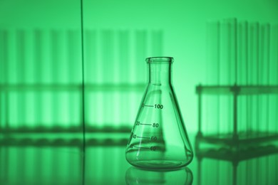 Photo of Empty flask on mirror surface against green background. Laboratory equipment