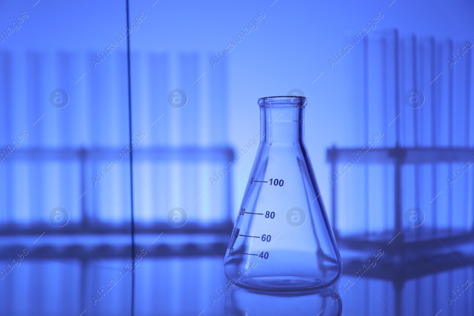 Photo of Empty flask on mirror surface against blue background. Laboratory equipment