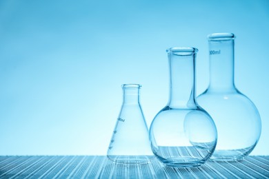 Empty flasks on table against light blue background, space for text. Laboratory equipment