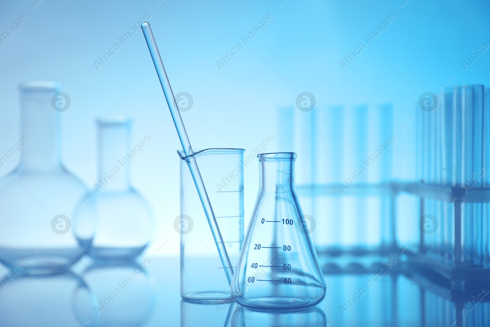 Photo of Laboratory glassware on mirror surface against light blue background