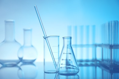 Photo of Laboratory glassware on mirror surface against light blue background