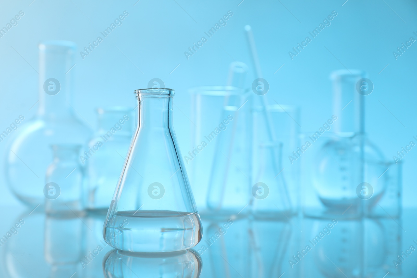 Photo of Flask with liquid and other laboratory glassware on mirror surface against light blue background