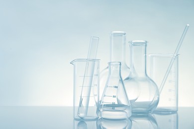 Laboratory glassware on mirror surface against light background, space for text