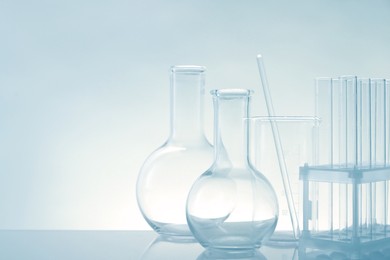 Photo of Laboratory glassware on mirror surface against light background, space for text