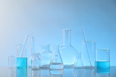 Photo of Laboratory glassware on mirror surface against light blue background