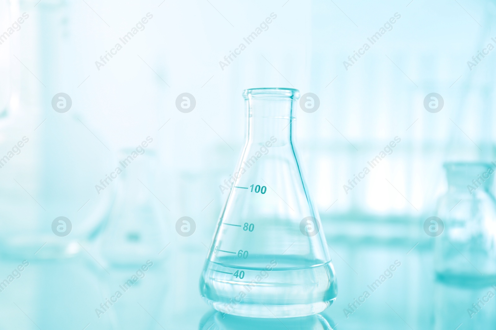 Photo of Flask with liquid on mirror surface against light background. Laboratory glassware