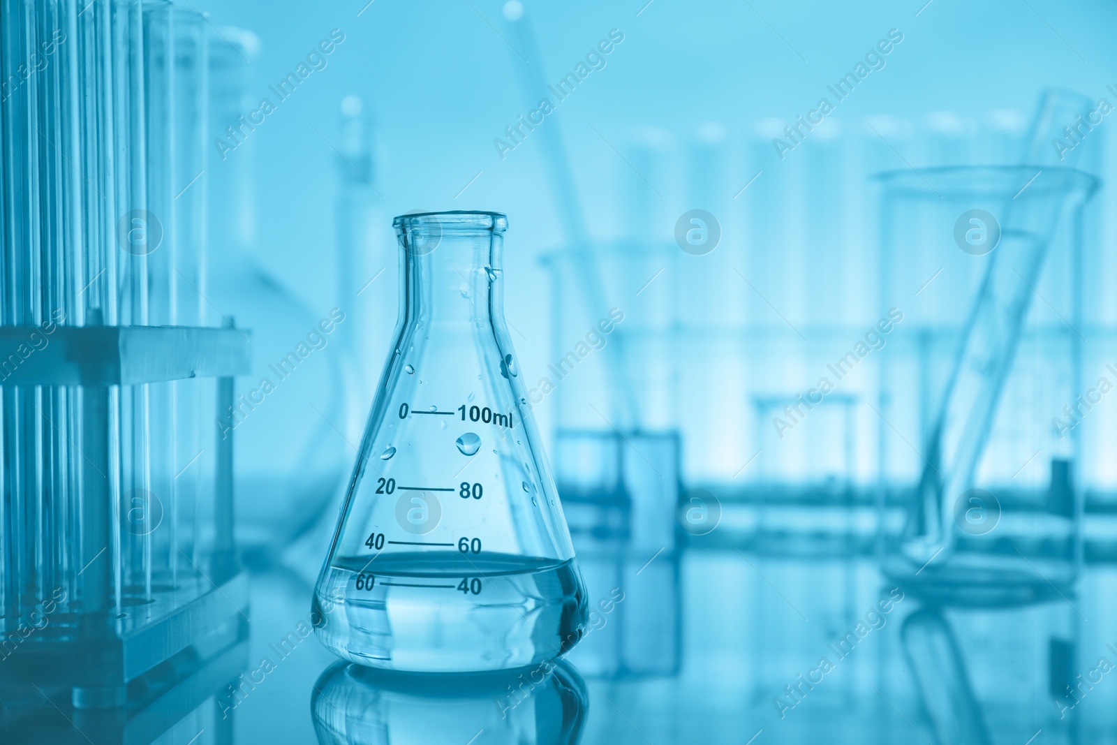 Photo of Laboratory glassware on mirror surface against turquoise background