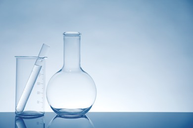 Laboratory glassware with liquid on mirror surface against light background, space for text