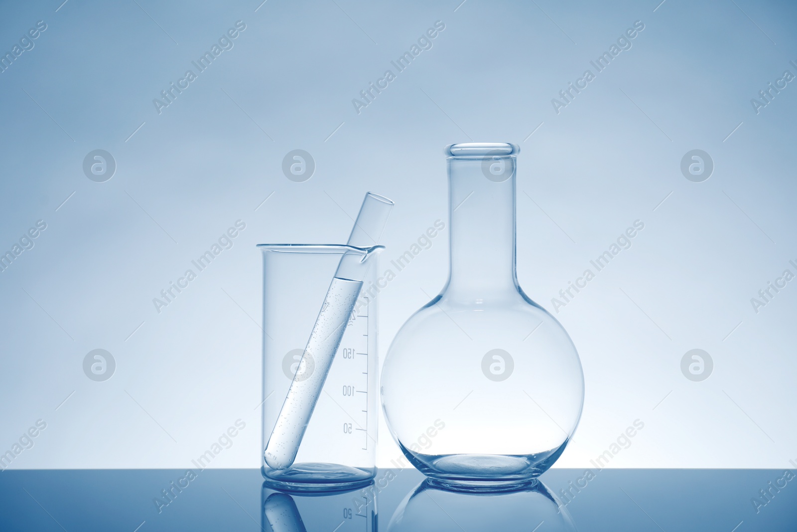 Photo of Laboratory glassware with liquid on mirror surface against light background