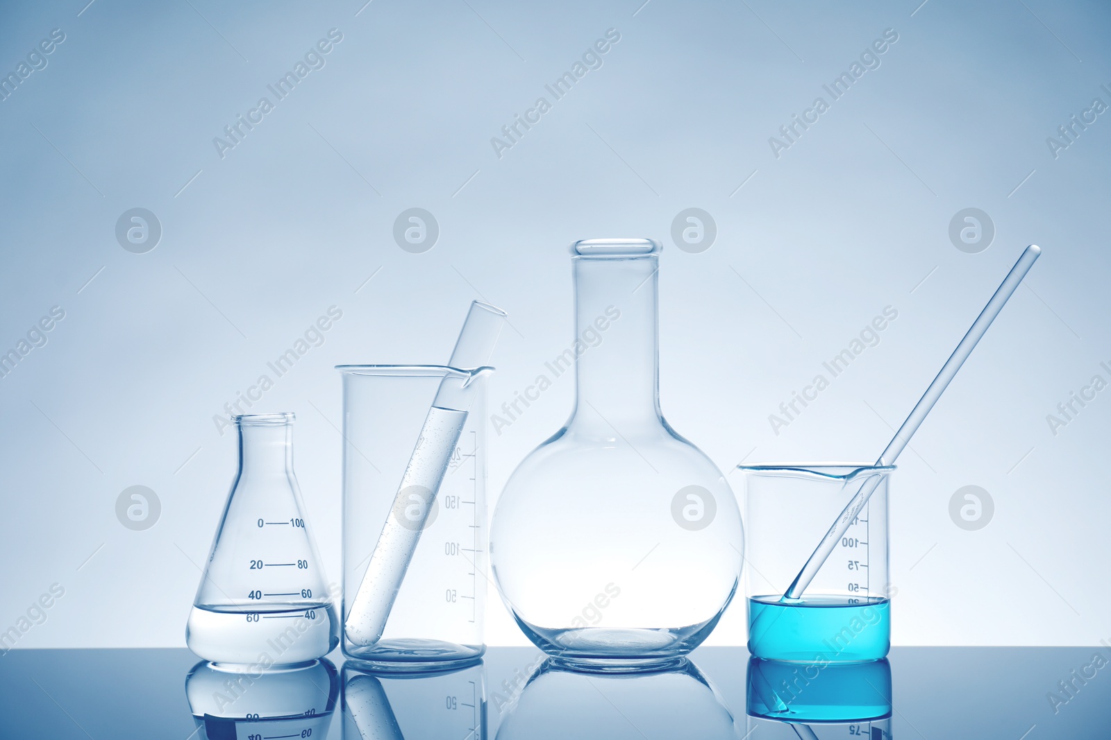 Photo of Laboratory glassware with liquid on mirror surface against light background