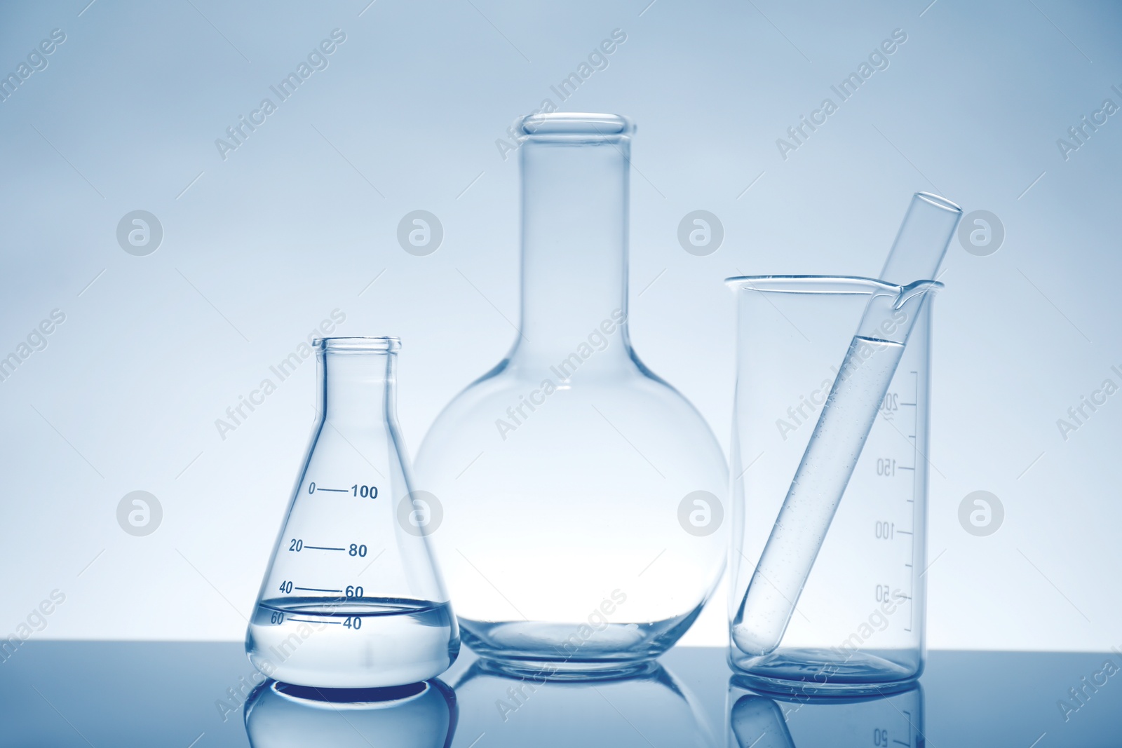 Photo of Laboratory glassware with liquid on mirror surface against light background