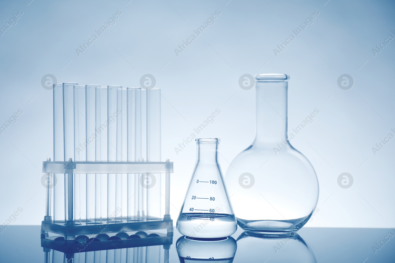 Photo of Laboratory glassware with liquid on mirror surface against light background