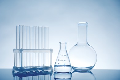 Photo of Laboratory glassware with liquid on mirror surface against light background