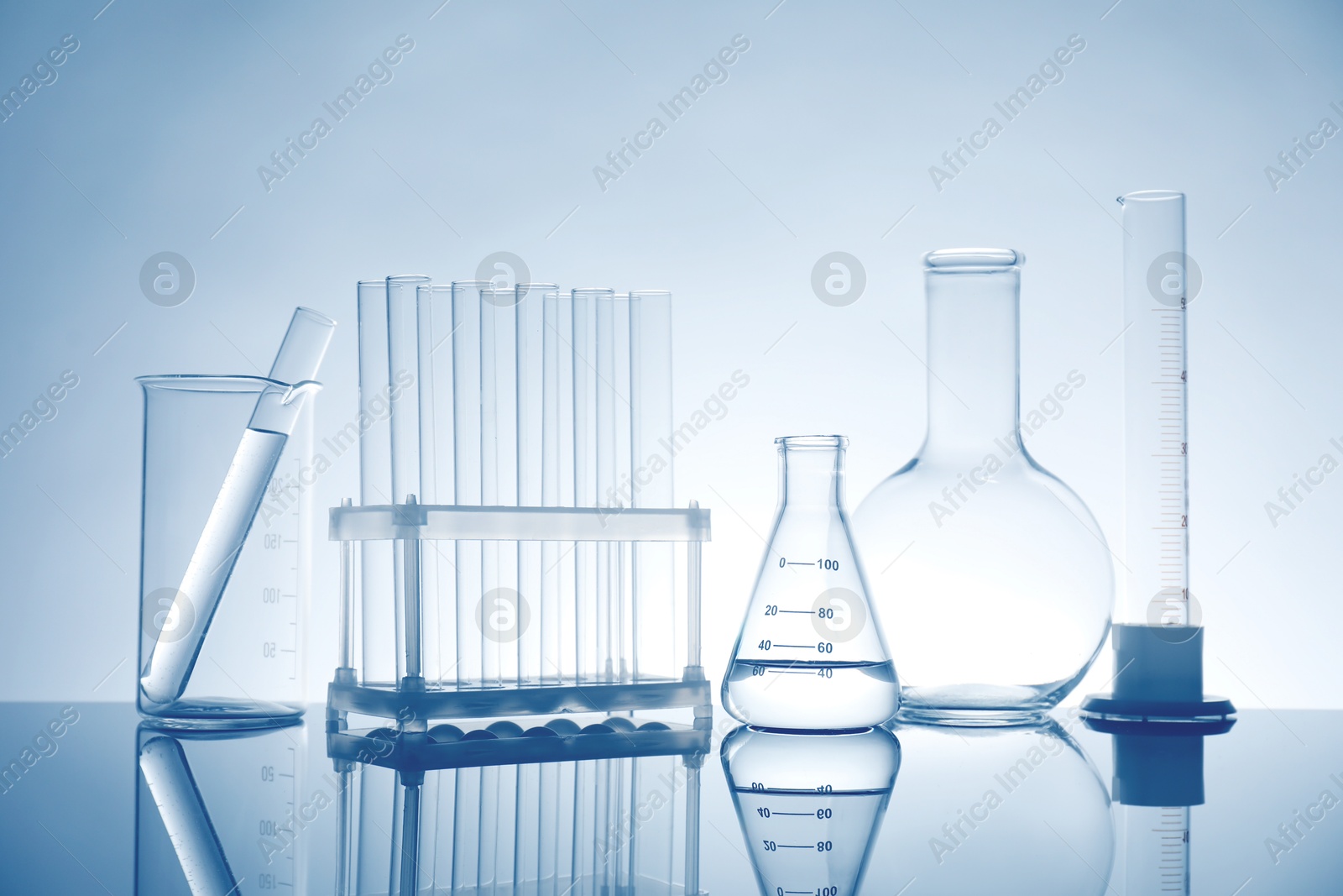 Photo of Laboratory glassware with liquid on mirror surface against light background