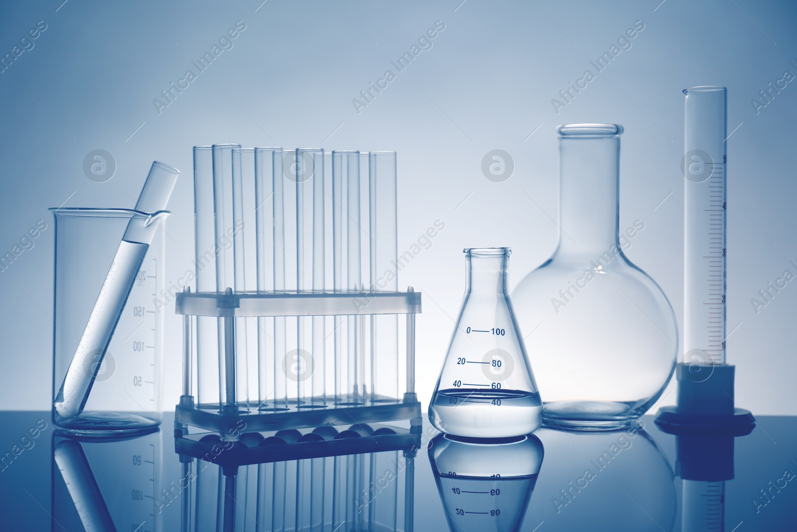 Photo of Laboratory glassware with liquid on mirror surface against light background