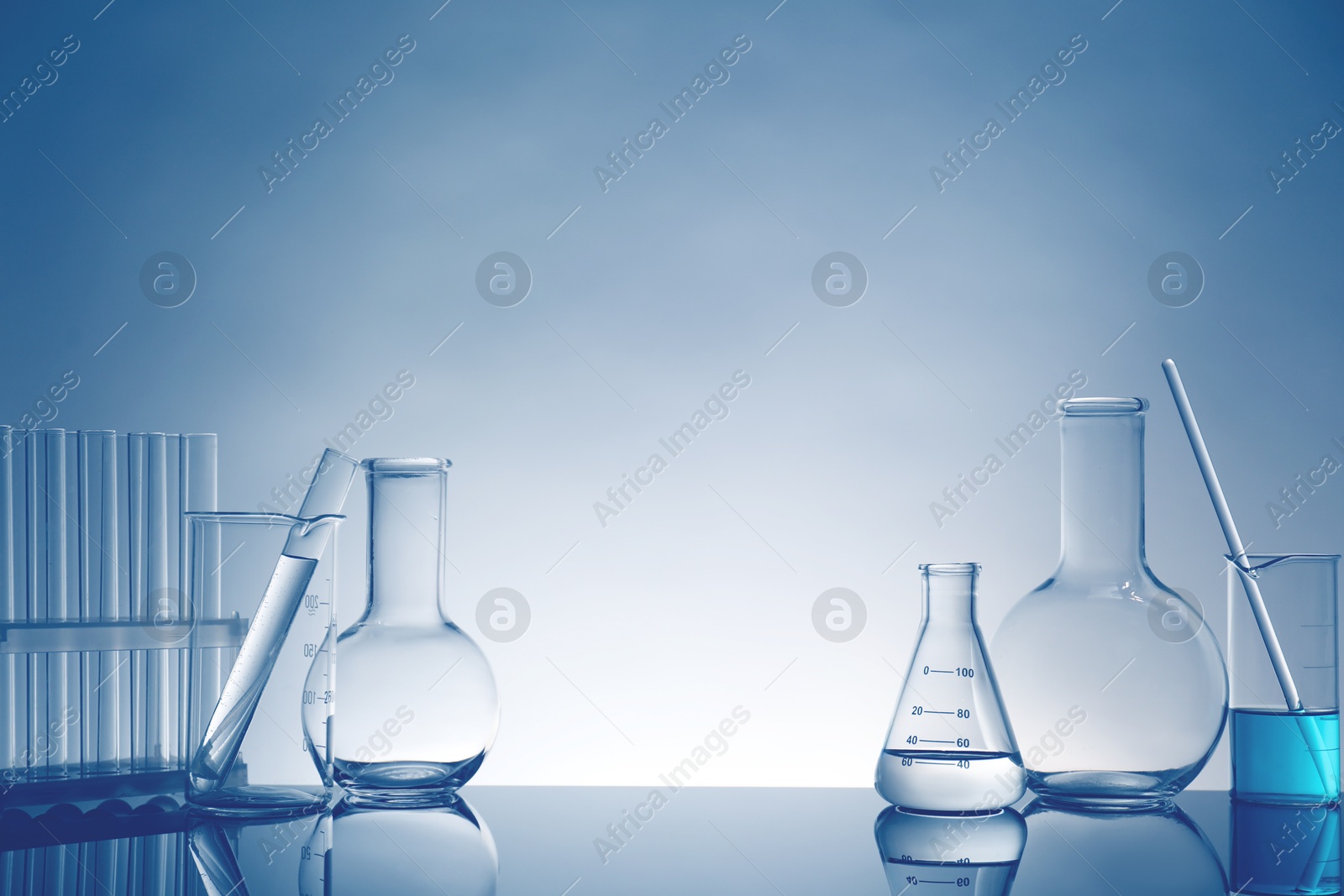 Photo of Laboratory glassware with liquid on mirror surface against light background