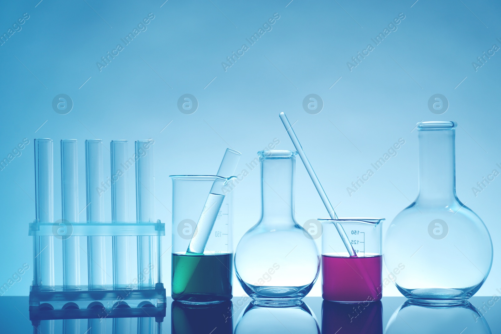 Photo of Laboratory glassware with liquid on mirror surface against light background