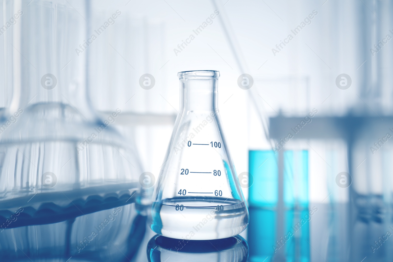 Photo of Laboratory glassware with liquid on mirror surface against light background