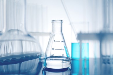 Photo of Laboratory glassware with liquid on mirror surface against light background