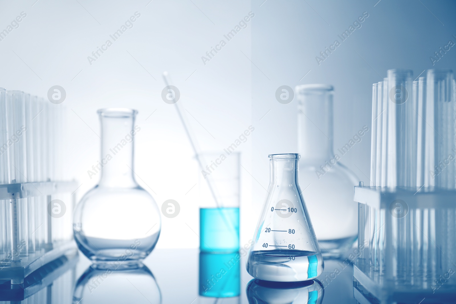 Photo of Laboratory glassware with liquid on mirror surface against light background