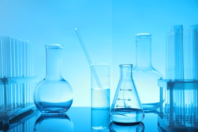 Photo of Laboratory glassware with liquid on mirror surface against light blue background