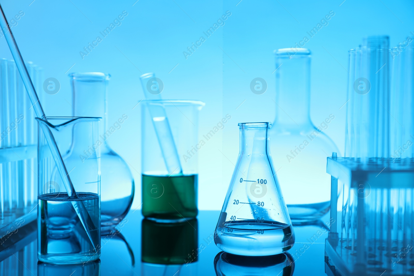 Photo of Laboratory glassware with liquid on mirror surface against light blue background