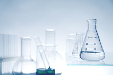 Photo of Flasks with liquid on glass surface and other laboratory glassware against light background