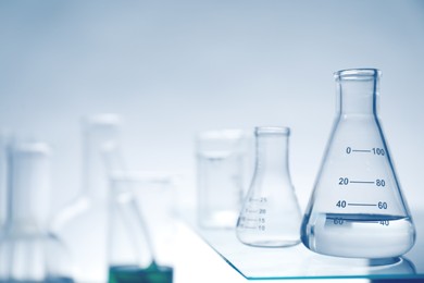 Flasks with liquid on glass surface and other laboratory glassware against light background