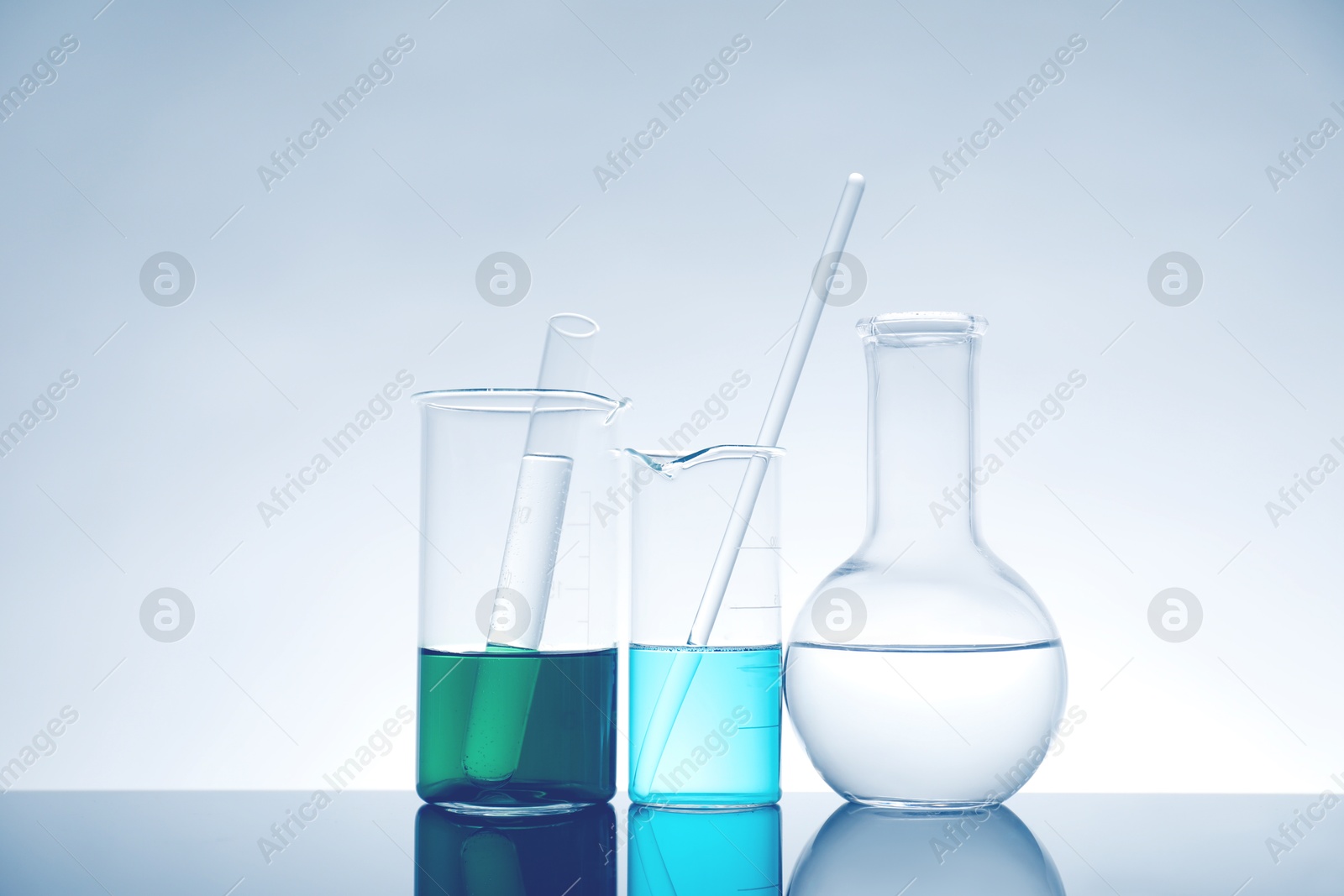 Photo of Laboratory glassware with liquid on mirror surface against light background