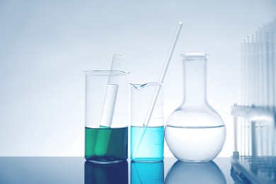 Photo of Laboratory glassware with liquid on mirror surface against light background