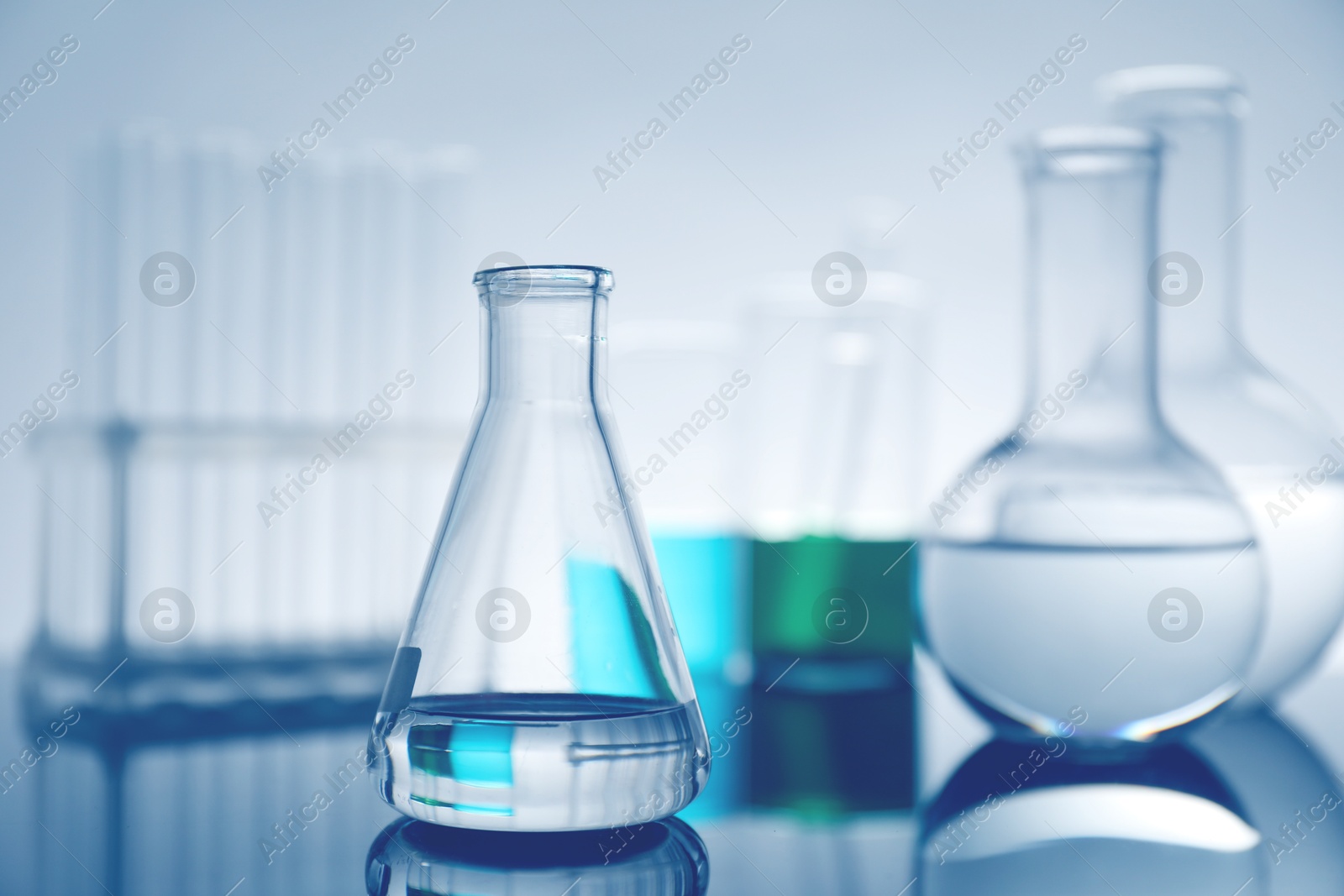 Photo of Laboratory glassware with liquid on mirror surface against light background