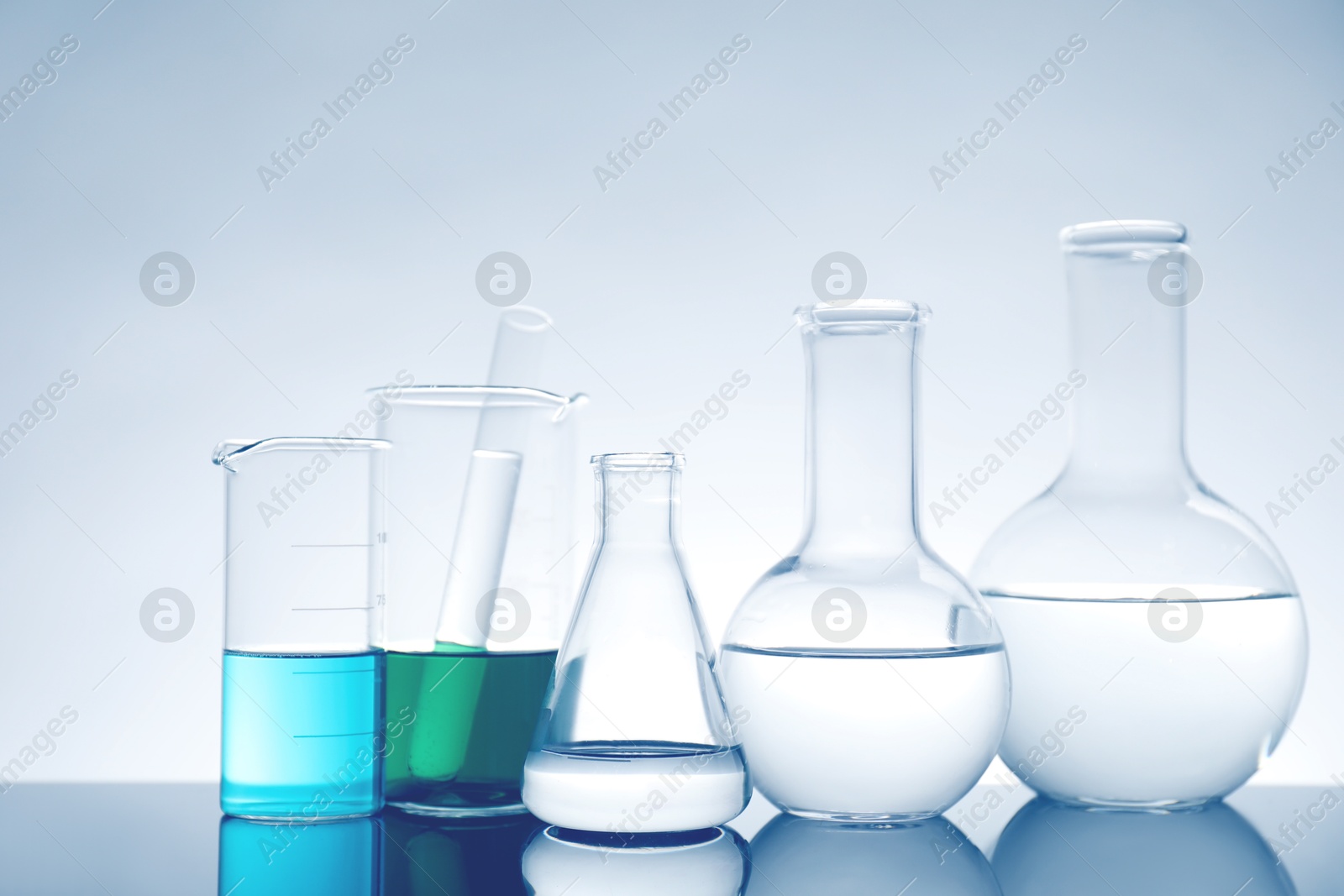 Photo of Laboratory glassware with liquid on mirror surface against light background