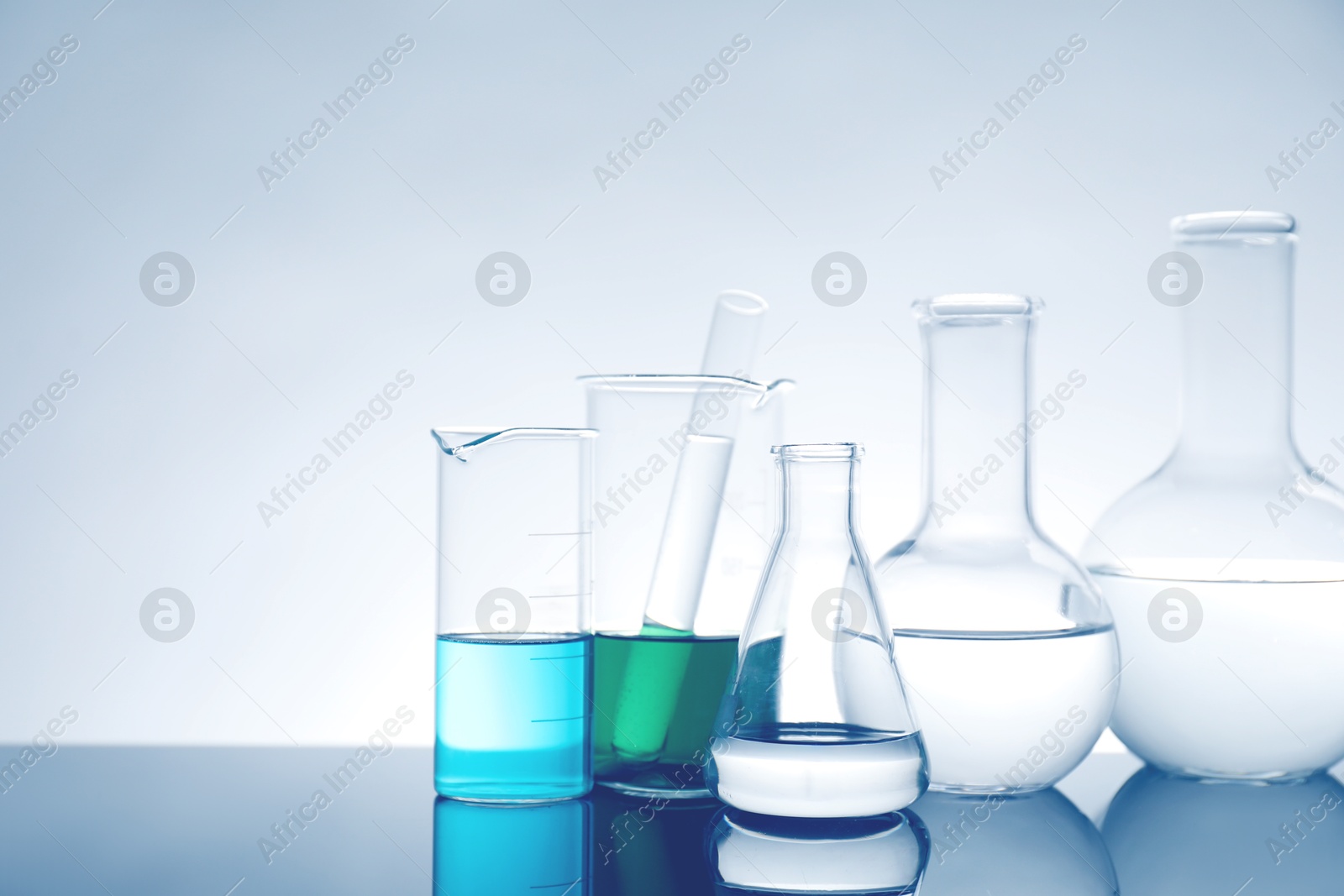 Photo of Laboratory glassware with liquid on mirror surface against light background, space for text