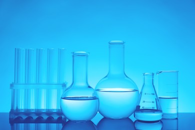 Laboratory glassware with liquid on mirror surface against light blue background