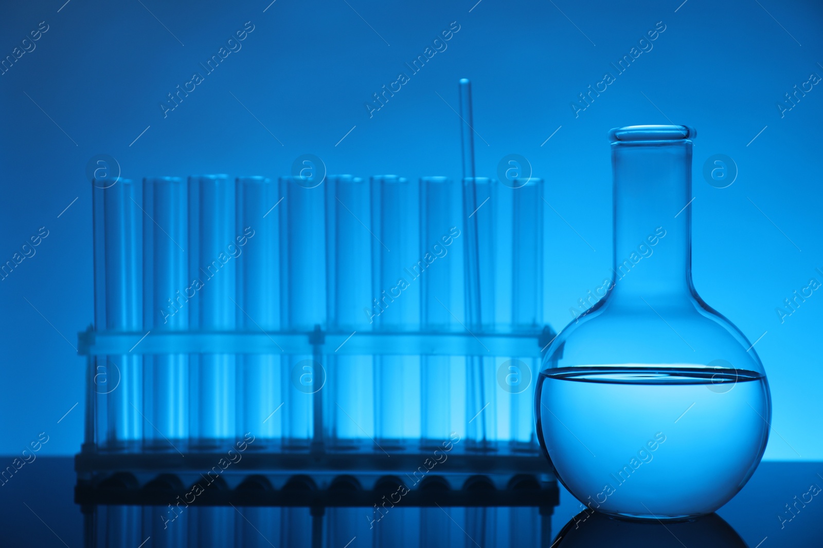 Photo of Laboratory glassware with liquid on mirror surface against light blue background