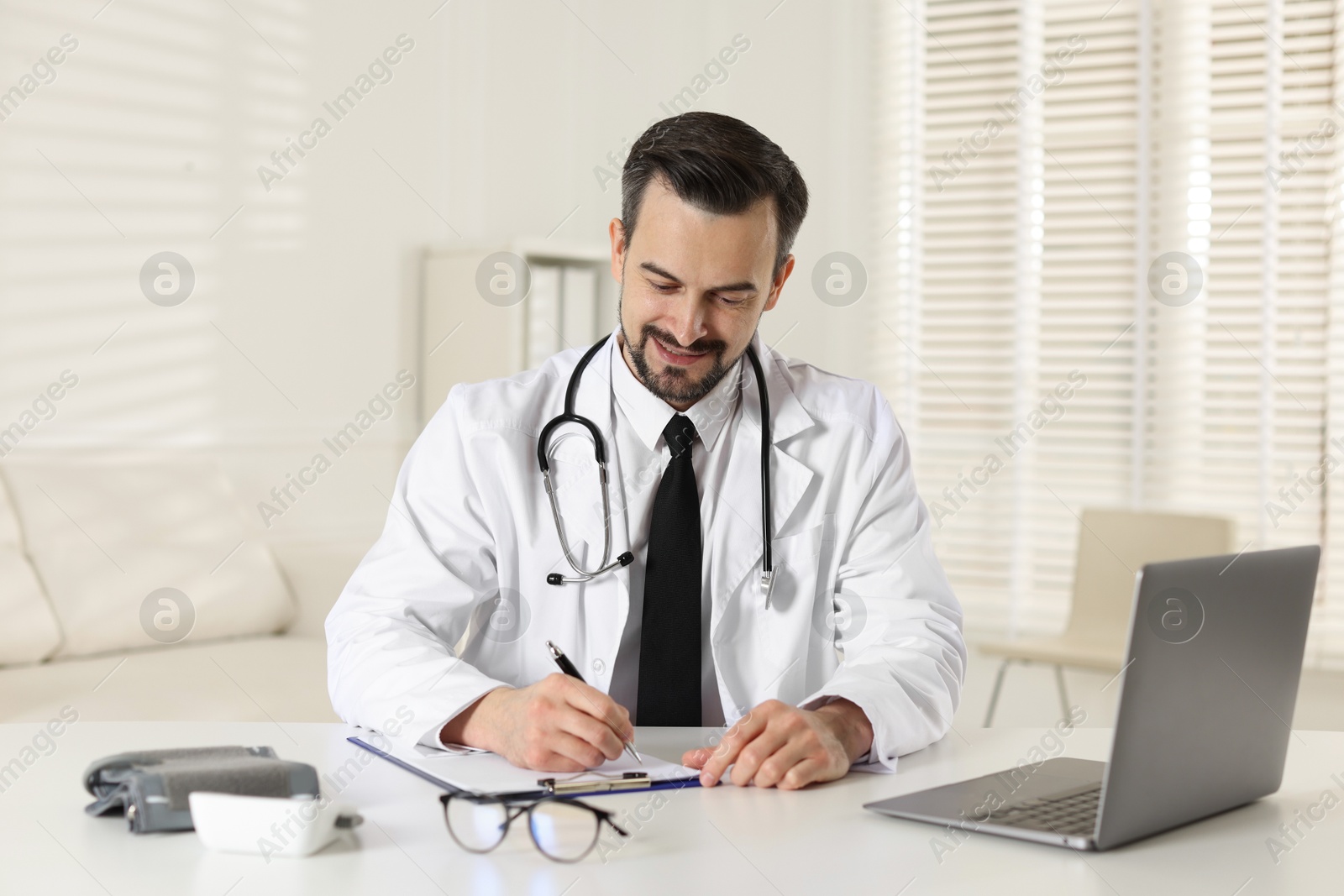 Photo of Cardiologist with stethoscope working at white table in clinic