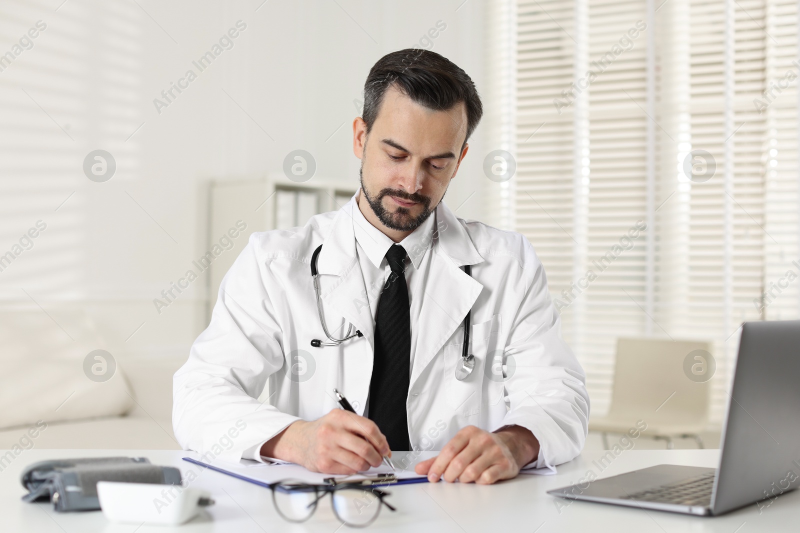 Photo of Cardiologist with stethoscope working at white table in clinic