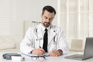 Cardiologist with stethoscope working at white table in clinic