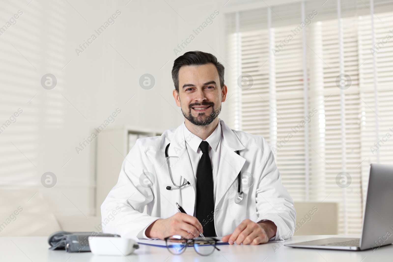 Photo of Cardiologist with stethoscope working at white table in clinic