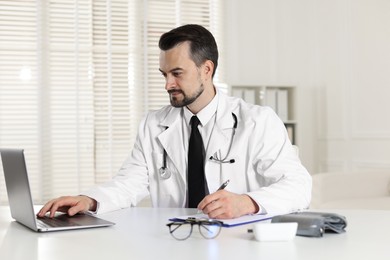 Photo of Cardiologist with stethoscope working at white table in clinic