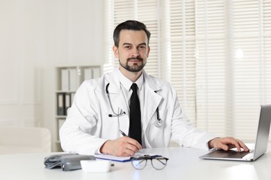 Photo of Cardiologist with stethoscope working at white table in clinic