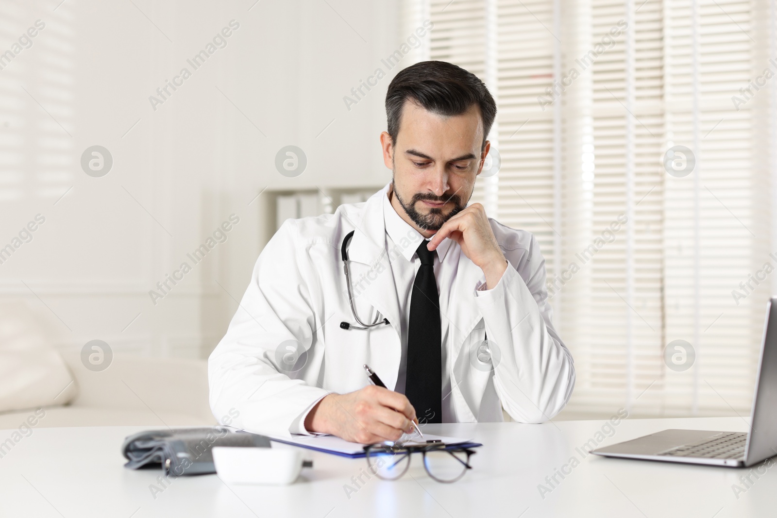 Photo of Cardiologist with stethoscope working at white table in clinic