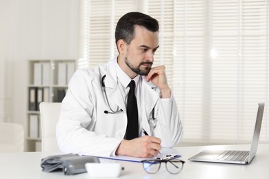 Photo of Cardiologist with stethoscope working at white table in clinic