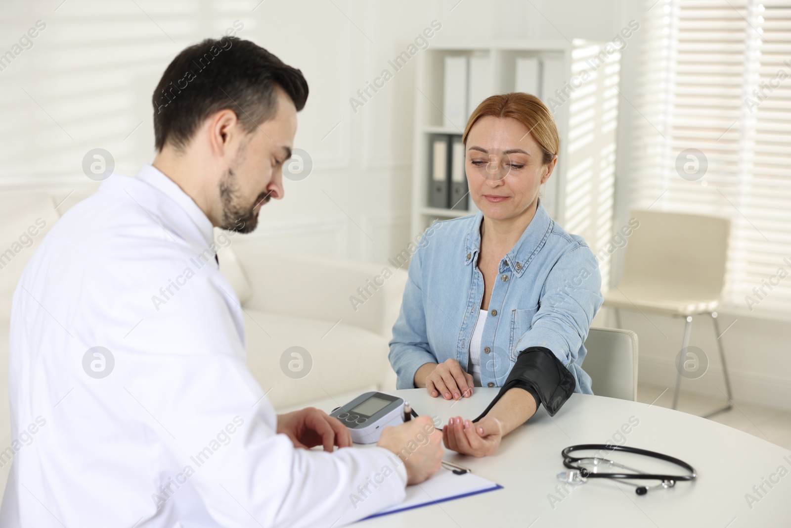 Photo of Cardiologist measuring patient's blood pressure at table in hospital