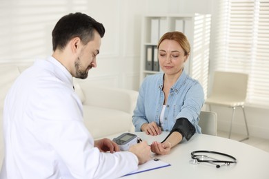 Cardiologist measuring patient's blood pressure at table in hospital