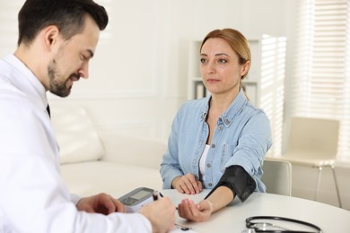 Cardiologist measuring patient's blood pressure at table in hospital