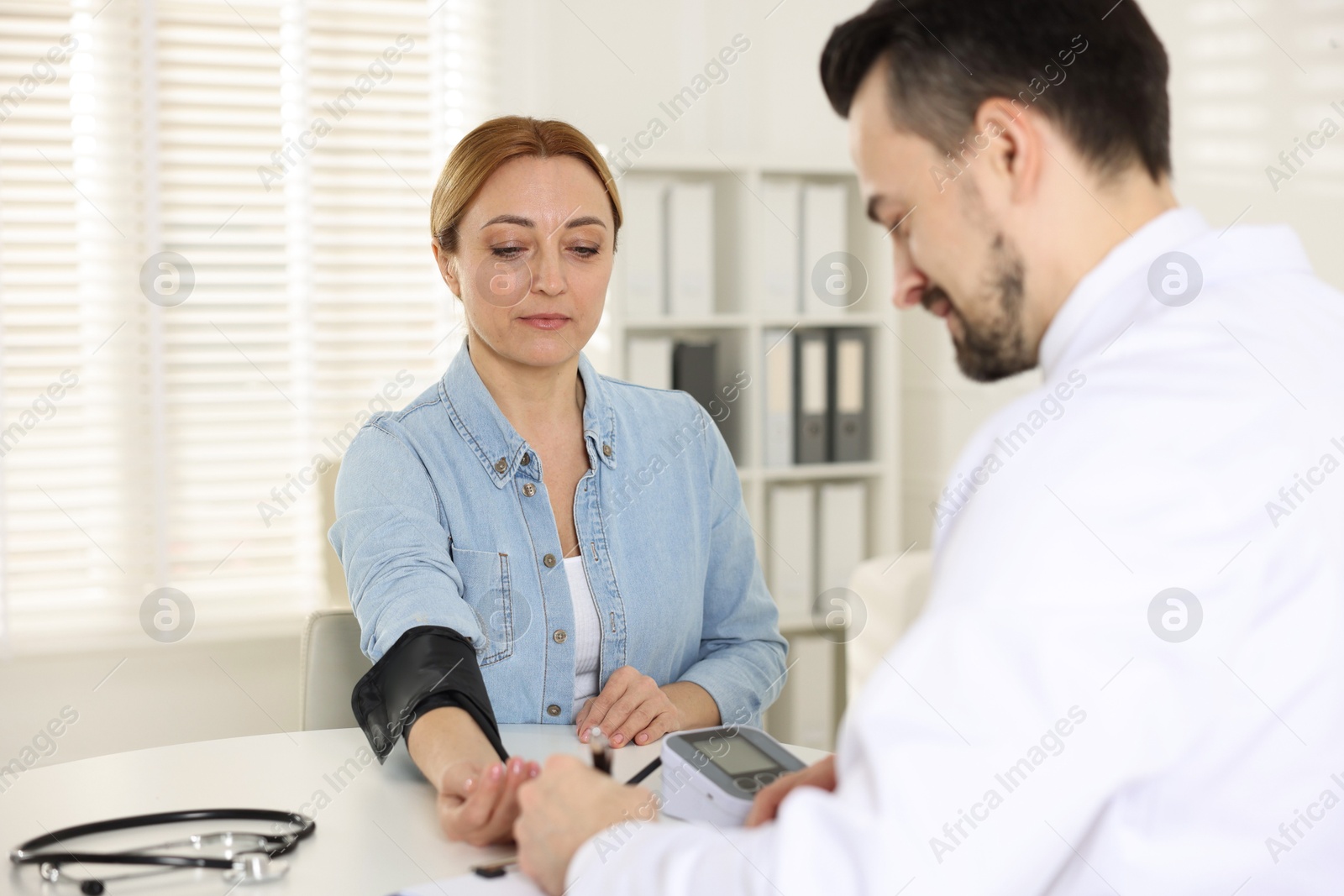 Photo of Cardiologist measuring patient's blood pressure at table in hospital