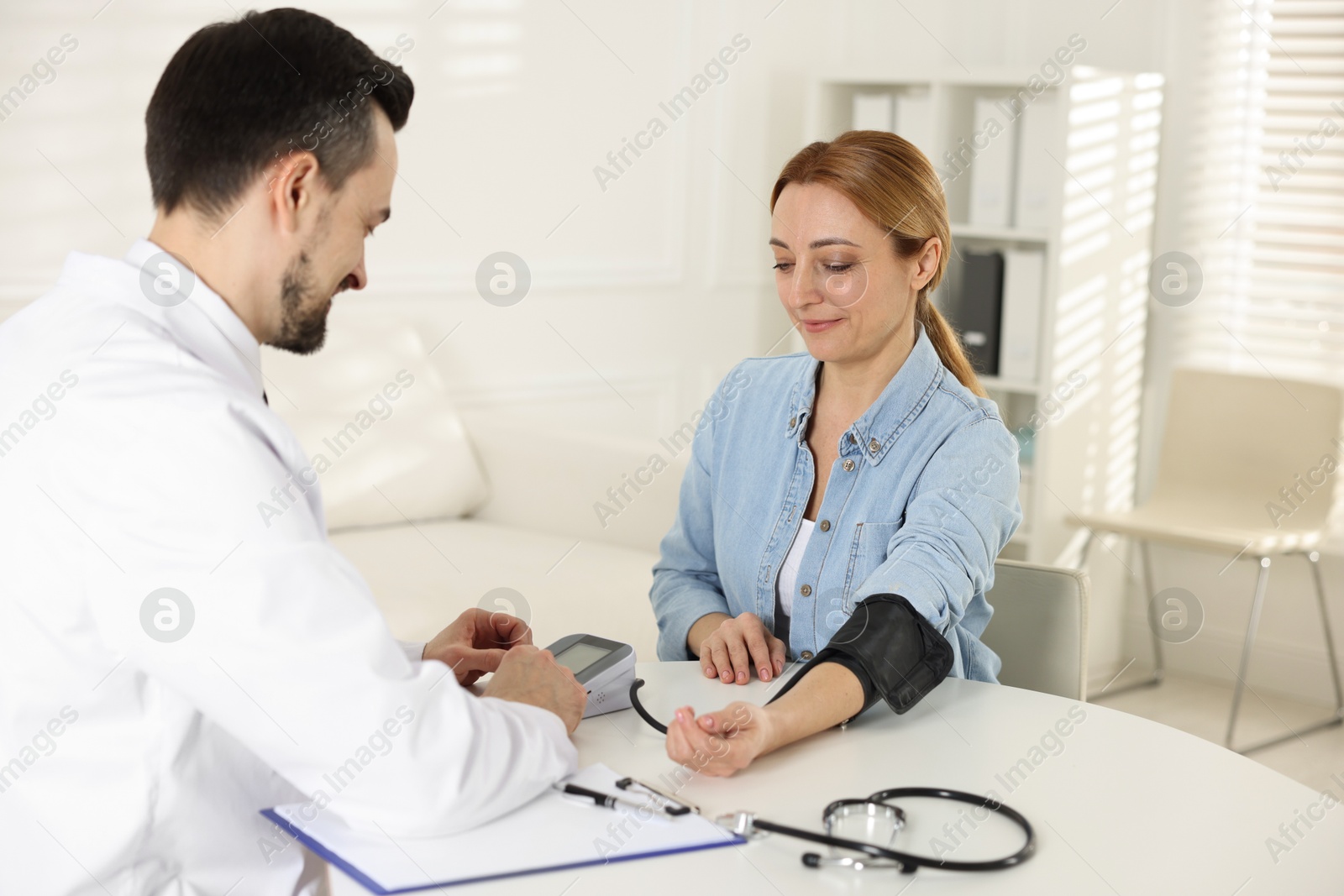 Photo of Cardiologist measuring patient's blood pressure at table in hospital