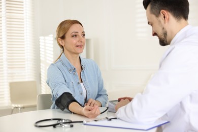 Cardiologist measuring patient's blood pressure at table in hospital